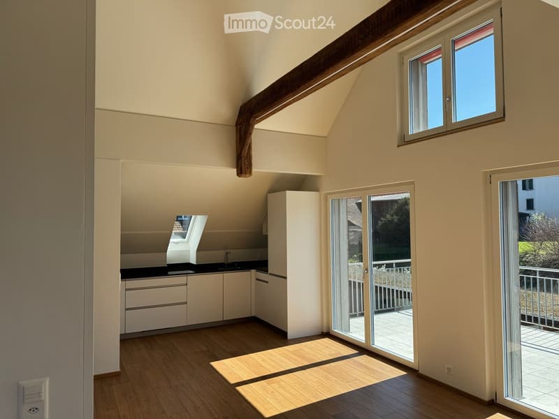 Bright, open room with wooden flooring, white kitchen cabinets, and a sliding glass door leading to a balcony.