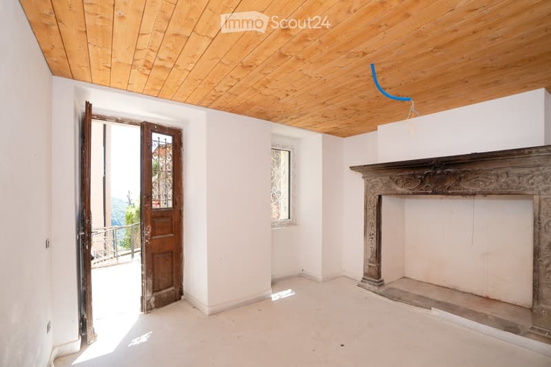 Empty room with white walls, wooden ceiling, fireplace, and open door leading to a balcony.