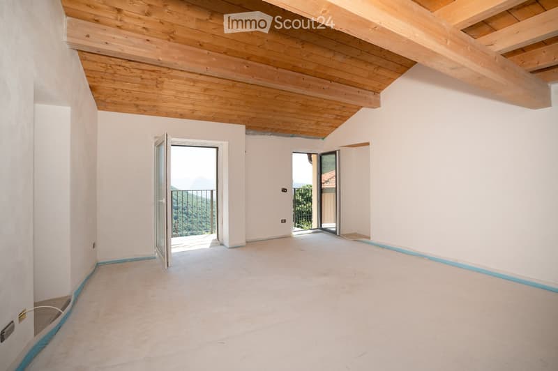 Empty room with white walls, wooden ceiling, and two open doors leading to a balcony with a scenic view.