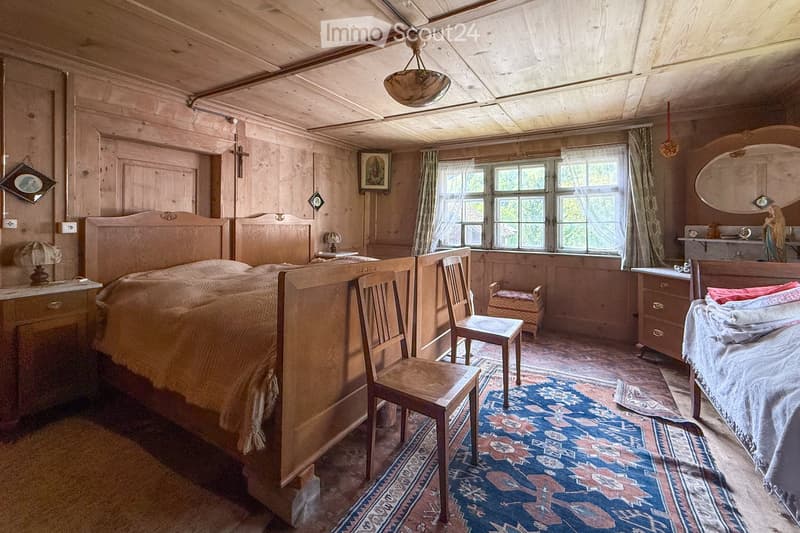 Bedroom with wooden beds, wooden walls and flooring, large windows, wooden chairs, rug, nightstand, lamp, table, picture frames, statue