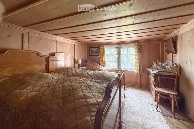 wooden room, double bed, desk with chair, window with curtains, small cabinet