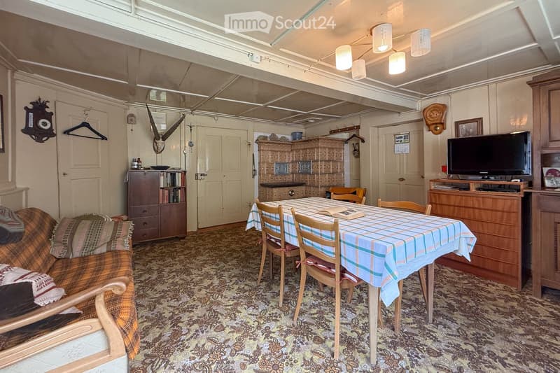 Interior with carpeted floor, dining table with chairs, couch, shelves, decorative objects, and cabinet with TV