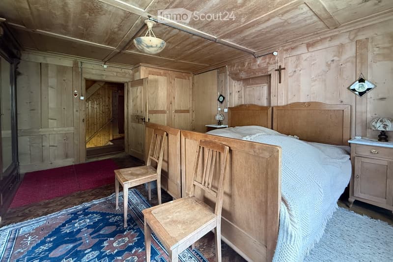 Room with wooden bed, two wooden chairs, a lamp, wooden wall and ceiling