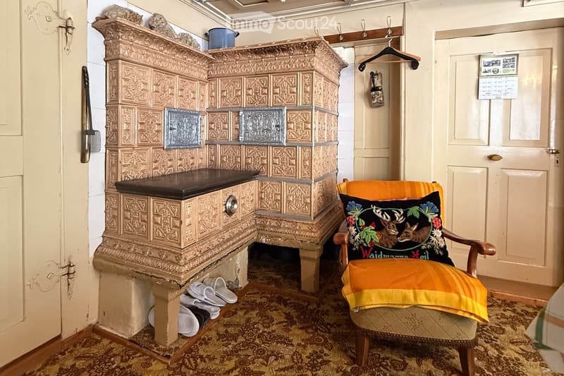 old ornate fireplace, pair of slippers under fireplace, patterned carpet, orange and yellow chair with pillow