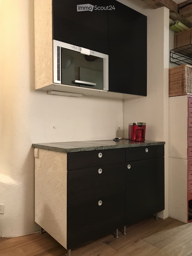 Modern kitchen with black cabinets, a built-in oven, and a granite countertop. A red coffee maker is placed on the counter.