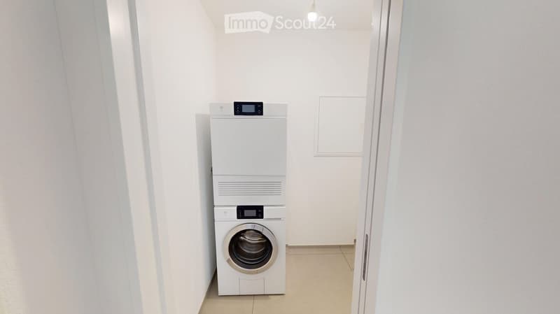 A small, clean room with a white washing machine and dryer stacked vertically, white walls, and a tiled floor.