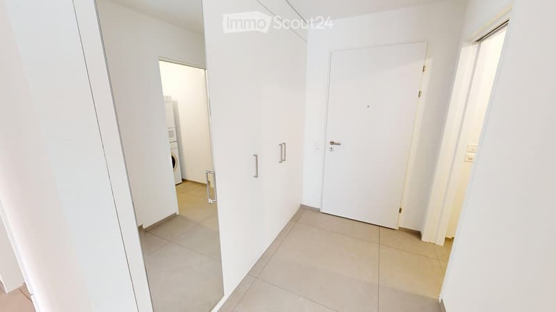 A clean, modern hallway with white walls, tiled flooring, and several doors leading to different rooms. A small closet is visible on the left side, and a washing machine is partially seen in an adjacent room.