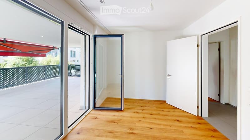 Empty room with wooden flooring, large sliding glass doors leading to a balcony, and white walls.