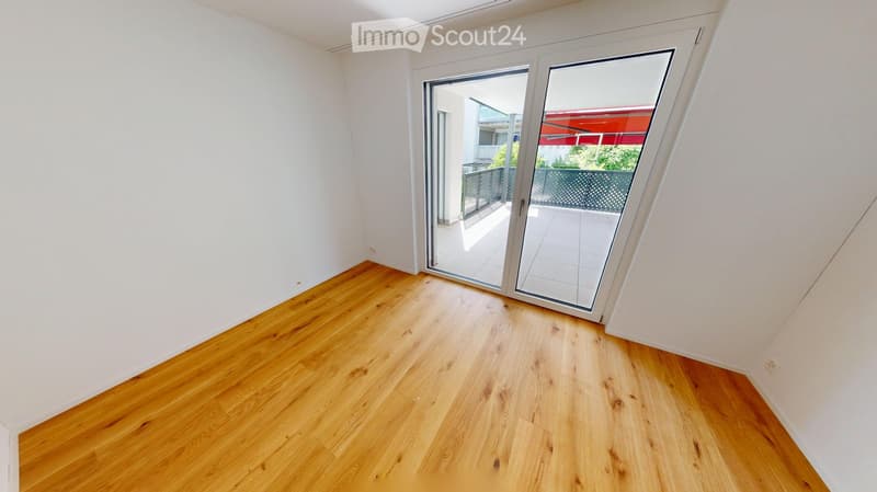 Empty room with light wooden flooring and white walls, featuring a large sliding glass door leading to a balcony.
