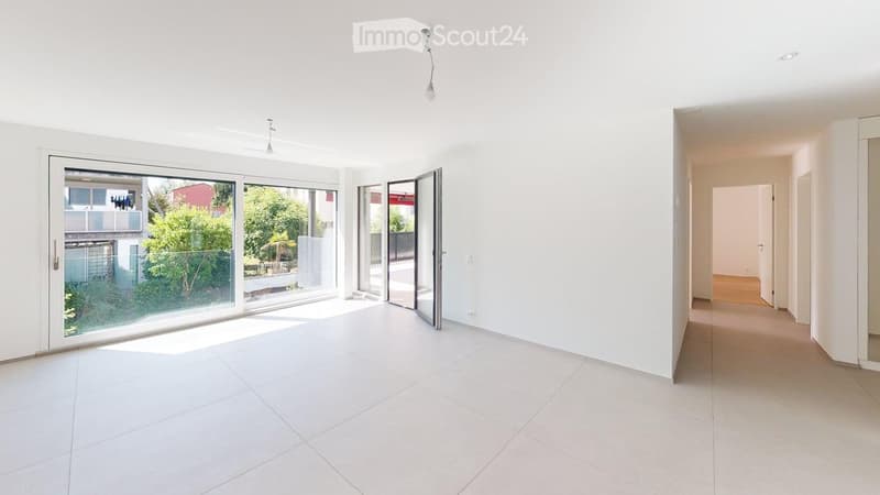 Empty room with white tiled floor, white walls, large sliding glass doors leading to outdoor area, and a hallway leading to another room.
