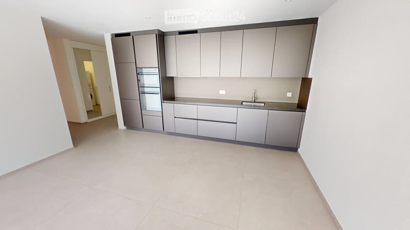 Empty kitchen with grey cabinets, a sink, and a tiled floor. The space is clean and unfurnished, with no appliances or furniture visible.