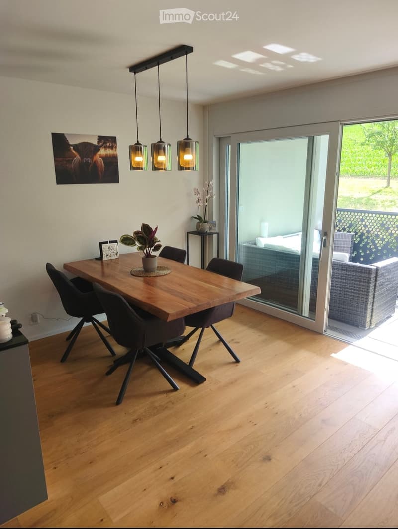 Modern dining room with wooden floor, large wooden dining table, pendant lights, and a view to the outdoor patio.