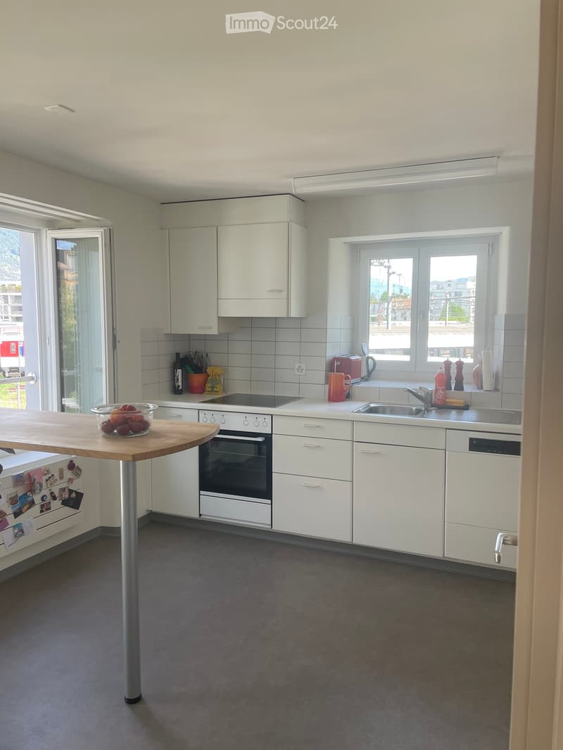 Modern kitchen with white cabinets, stainless steel appliances, and a wooden island table. Features include an oven, sink, and various kitchen items on the counters.