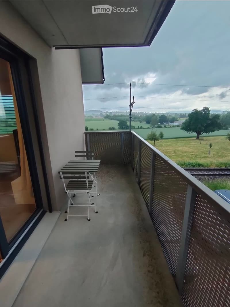Balcony with a table and chair, overlooking a rural landscape with fields and trees.