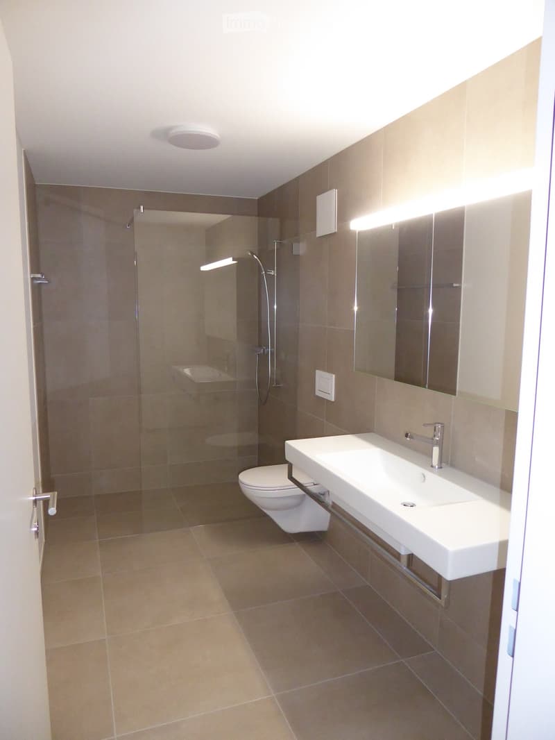 Bathroom. Modern bathroom with beige tiles, a white sink with a modern faucet, a toilet, a glass-enclosed shower, and a large mirror with built-in lighting.