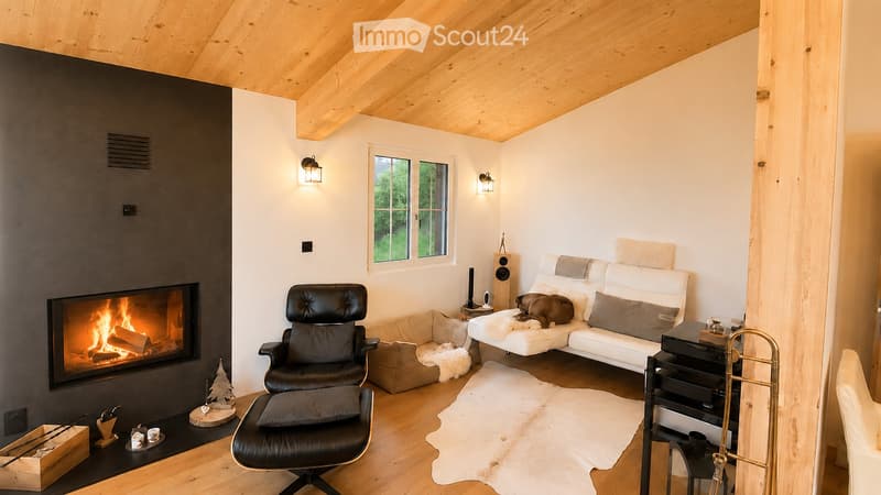 Modern living room with exposed wooden ceiling, fireplace, white sofa, black leather chair, and wooden floor.