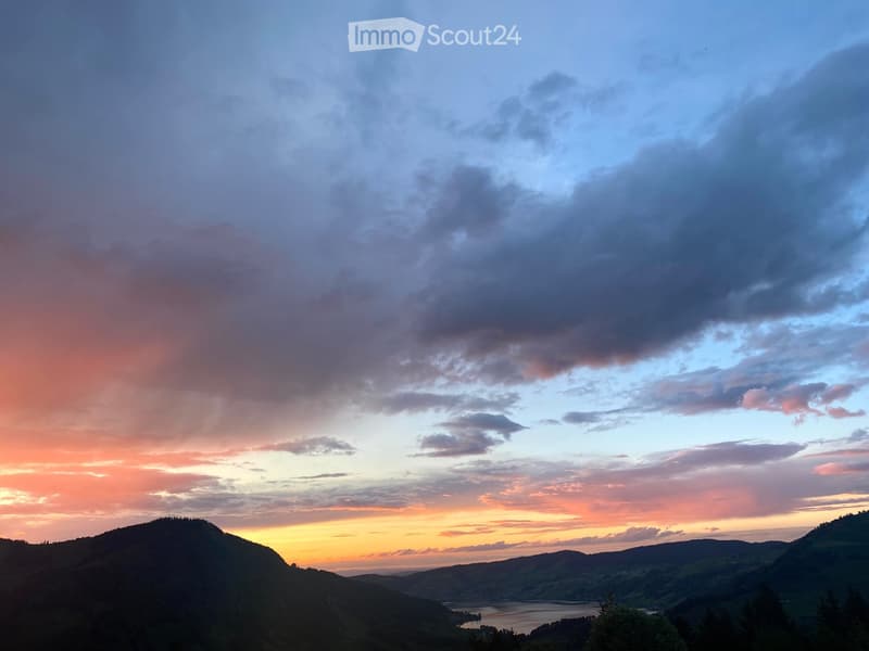Panoramic view of a valley at sunset, with rolling hills, a lake, and a colorful sky.