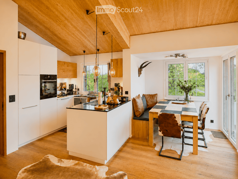 Open-plan kitchen and dining area with white cabinets, wooden ceiling, pendant lights, and a dining table with chairs.