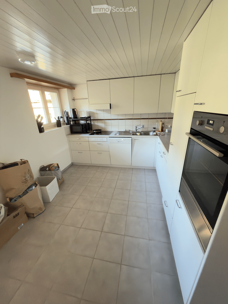 Bright kitchen with white cabinets, tiled floor, and modern appliances including an oven, microwave, and dishwasher. Natural light from a window on the left side.