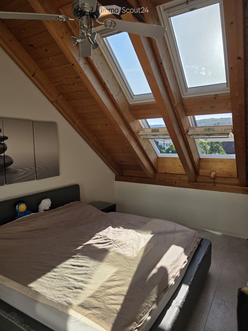 Bright attic bedroom with wooden slanted ceilings, skylights, a large bed, nightstand, and a ceiling fan.