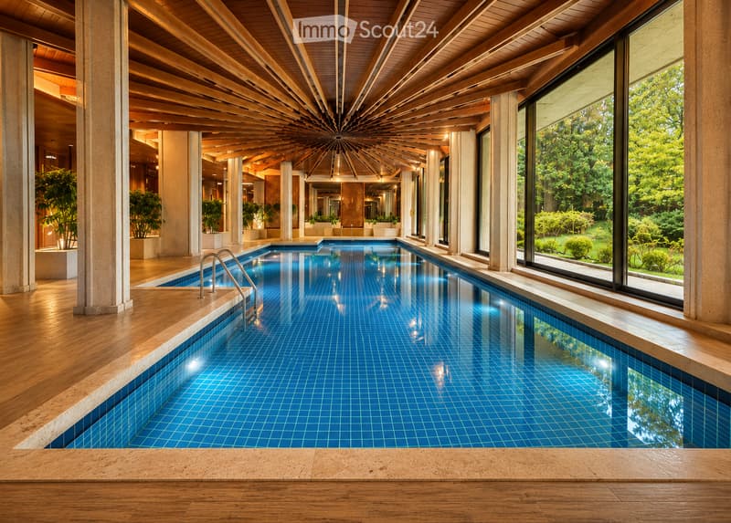 Indoor swimming pool area with large windows overlooking a lush garden, wooden flooring, and modern architectural design.