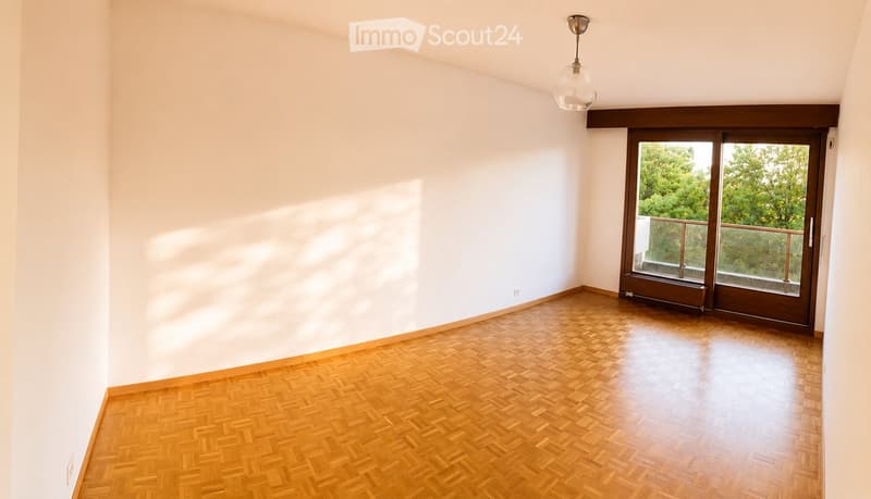 Empty room with wooden herringbone flooring, white walls, and a large sliding glass door leading to a balcony.