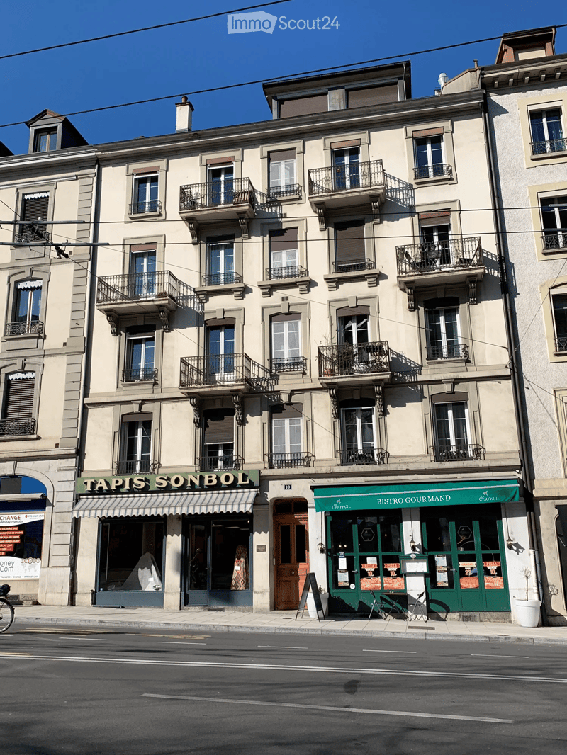 A multi-story building with beige facade, multiple windows, and balconies. Ground floor features two businesses: 'Tapis Sonbol' and 'Bistro Gourmand'.
