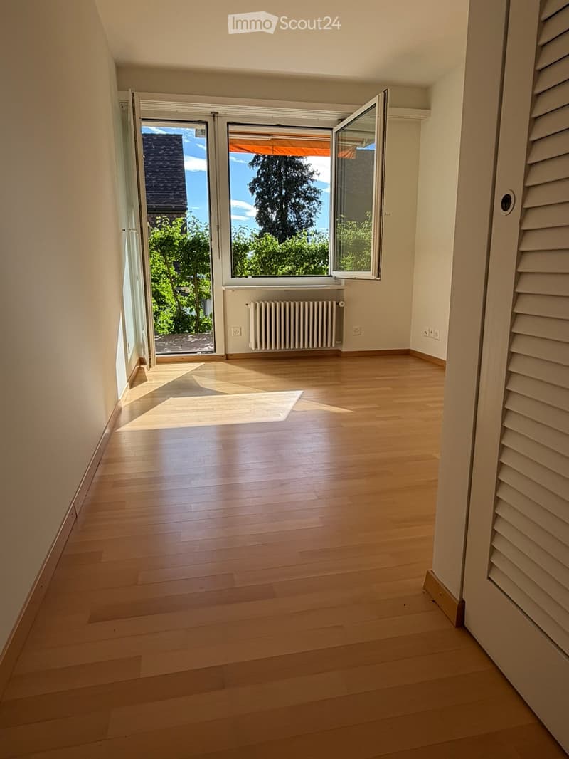 Empty room with wooden flooring, large windows, radiator, and natural light streaming in.