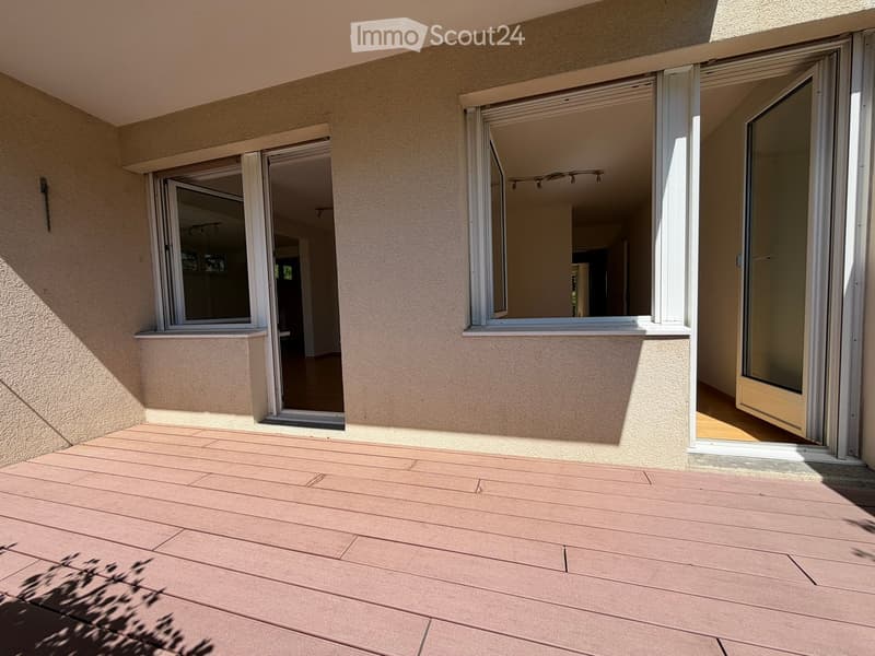Wooden deck with large sliding glass doors leading into the house, with visible interior lighting and flooring.