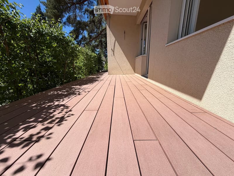 Wooden deck attached to a building, with a view of greenery and trees in the background.
