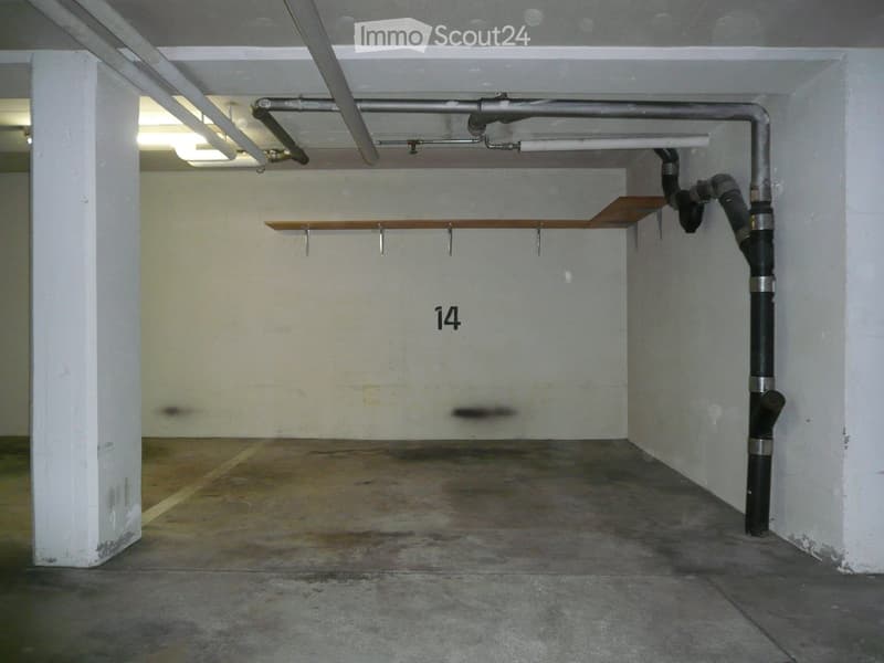 Empty underground parking space with concrete floor, white walls, and numbered stall14. Exposed pipes and lighting fixtures are visible.