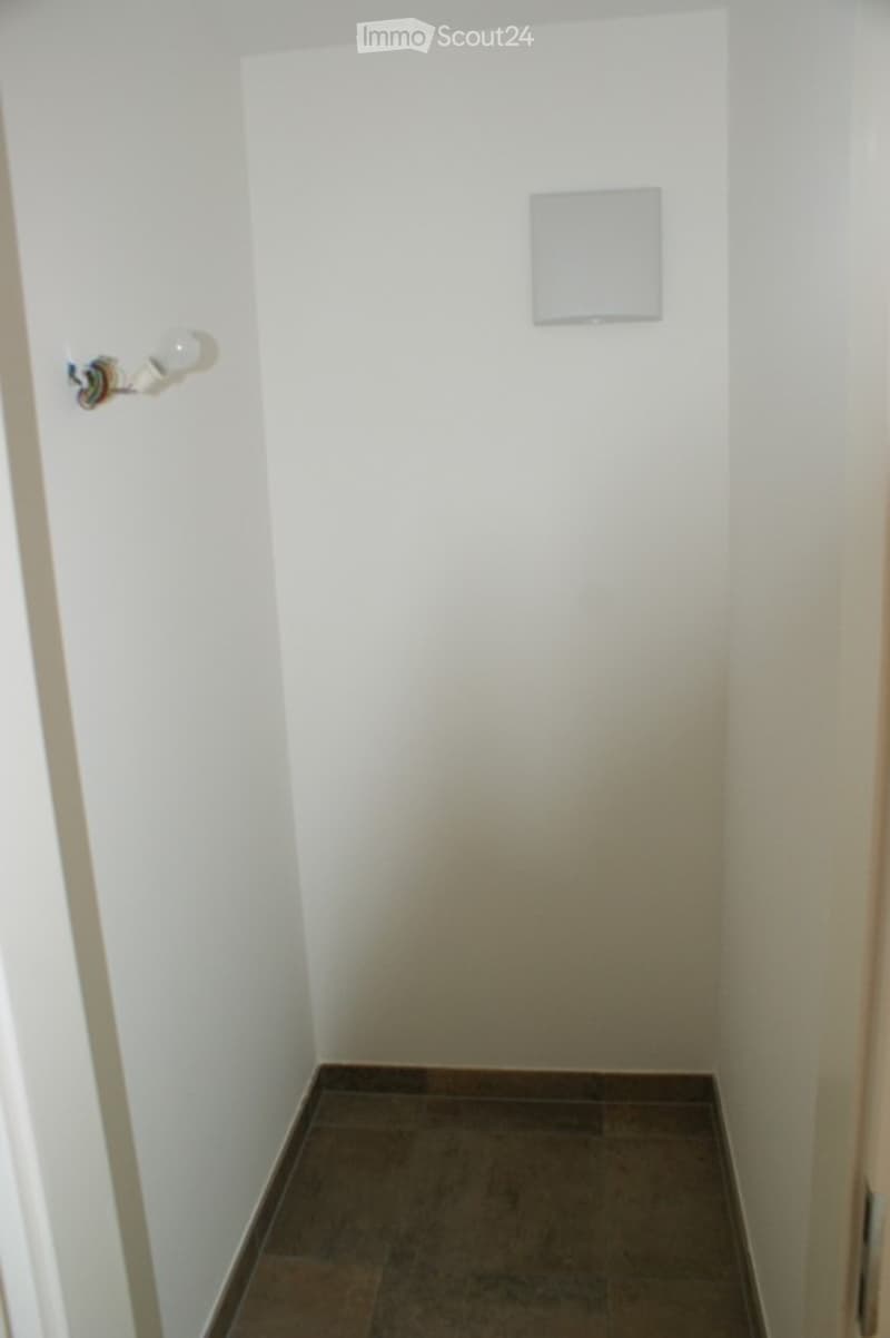 Empty room with white walls and dark tiled floor, featuring a light switch and a light fixture on the wall.