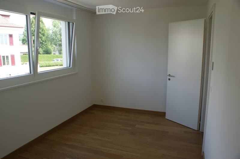 Empty room with wooden flooring, white walls, large window, and a closed door.