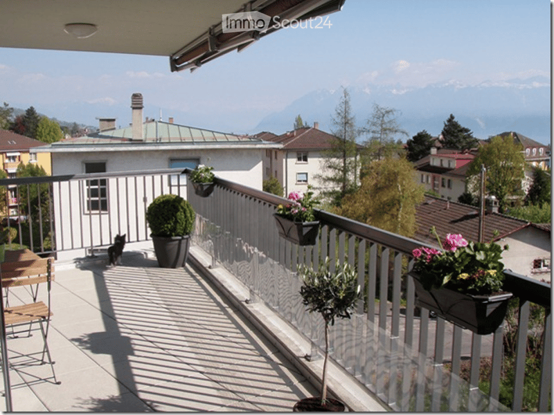 Balcony with metal railing, potted plants, and a view of the city and mountains.