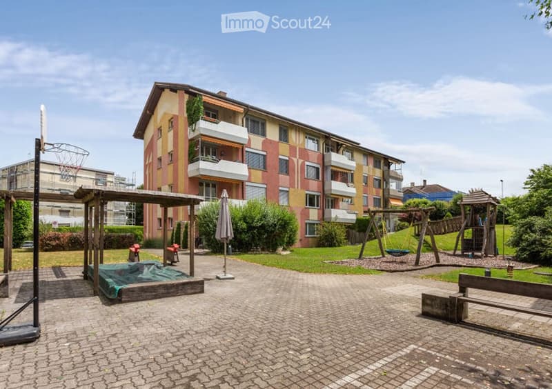 Courtyard area with playground equipment, benches, and a multi-story residential building in the background.