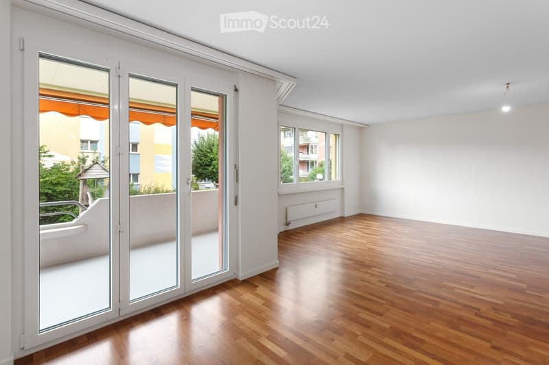 Empty room with wooden flooring, large sliding glass doors leading to a balcony, and white walls.