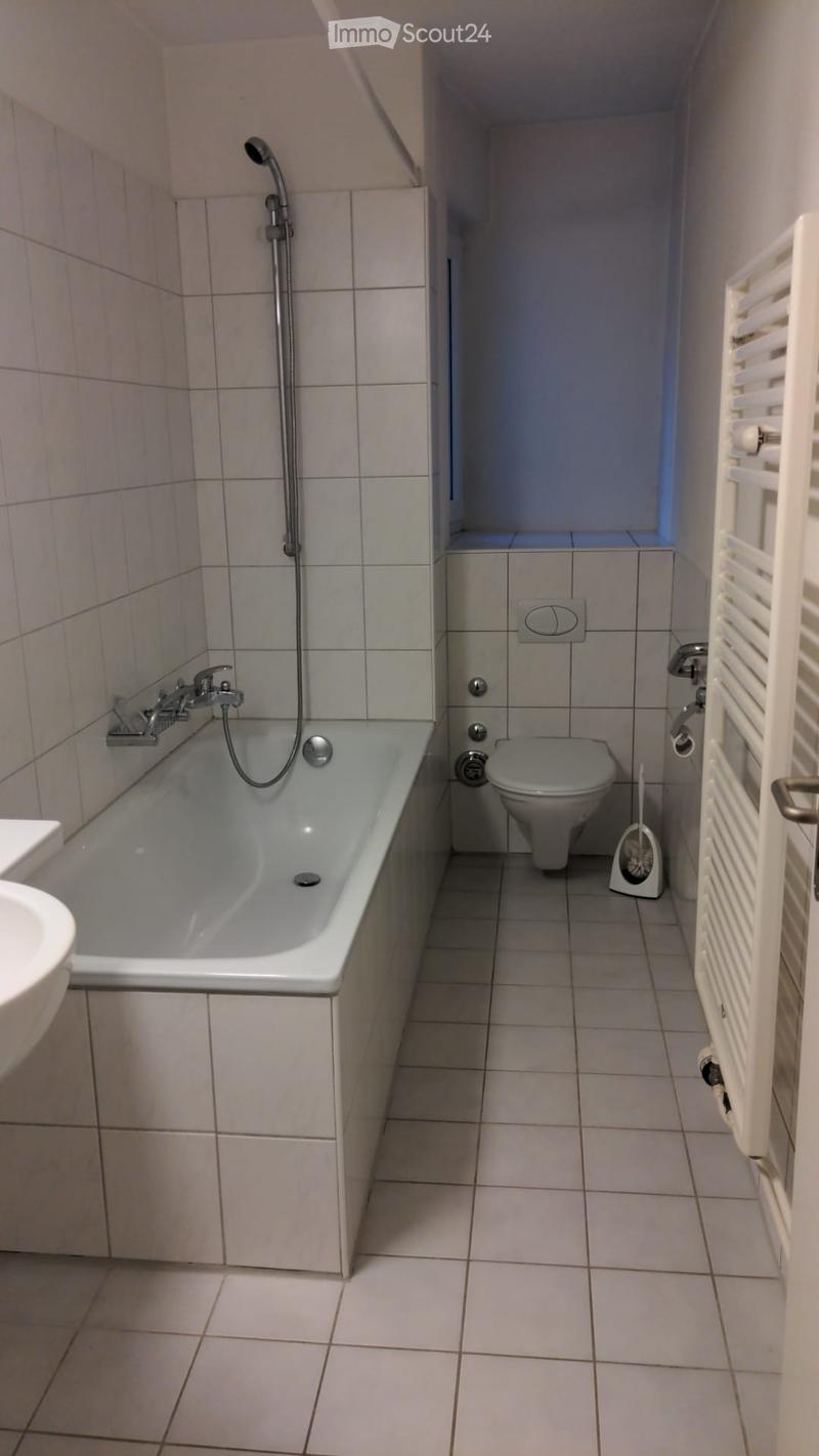 A small bathroom with a bathtub, toilet, and showerhead, featuring tiled walls and floor.