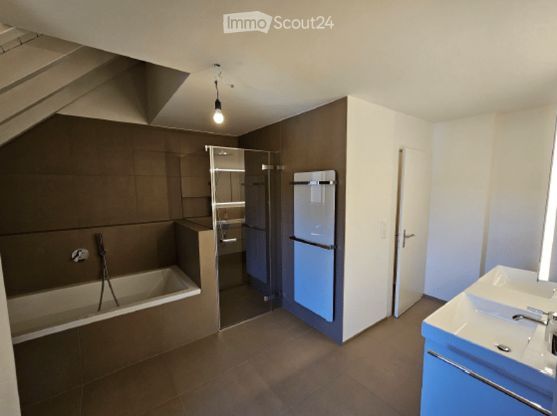 Modern bathroom with a bathtub, sink, and a small refrigerator. The space features tiled walls and a sleek, contemporary design.