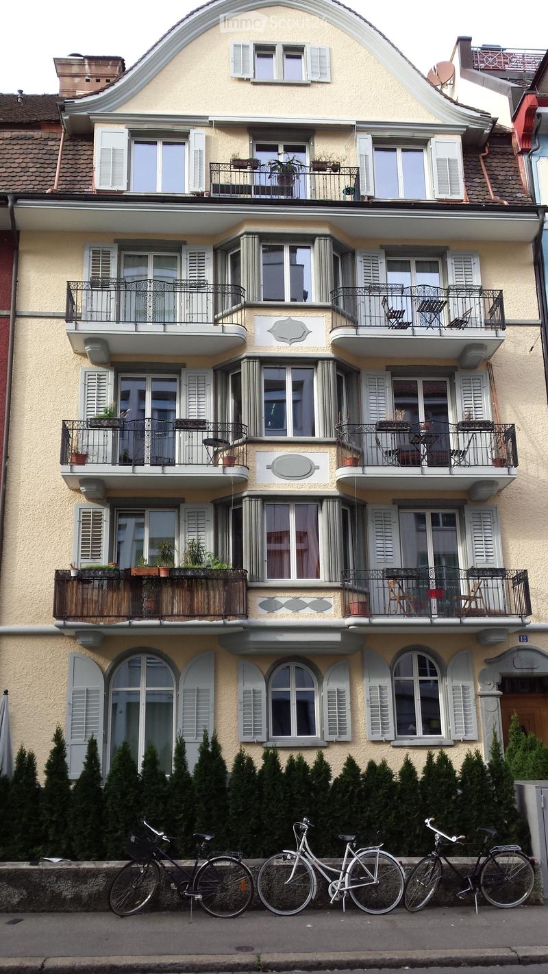 4 story building, beige paint, white shutters, balconies, windows, metal railings, potted plants