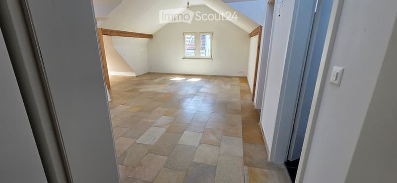 Empty attic space with exposed wooden beams, tiled floor, and a skylight window. No furniture or equipment present.