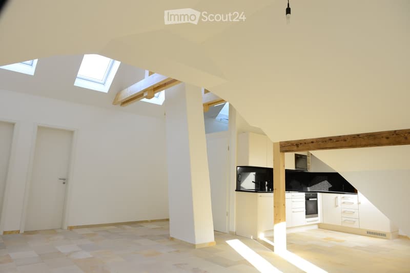 empty room, tiled floor, white walls, multiple attic windows, kitchen area, light fixtures