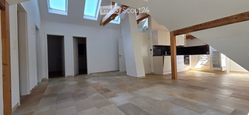 Bright, open-plan living and dining area with tiled flooring, white walls, and skylights. Adjacent modern kitchen features white cabinets, stainless steel appliances, and ample natural light.
