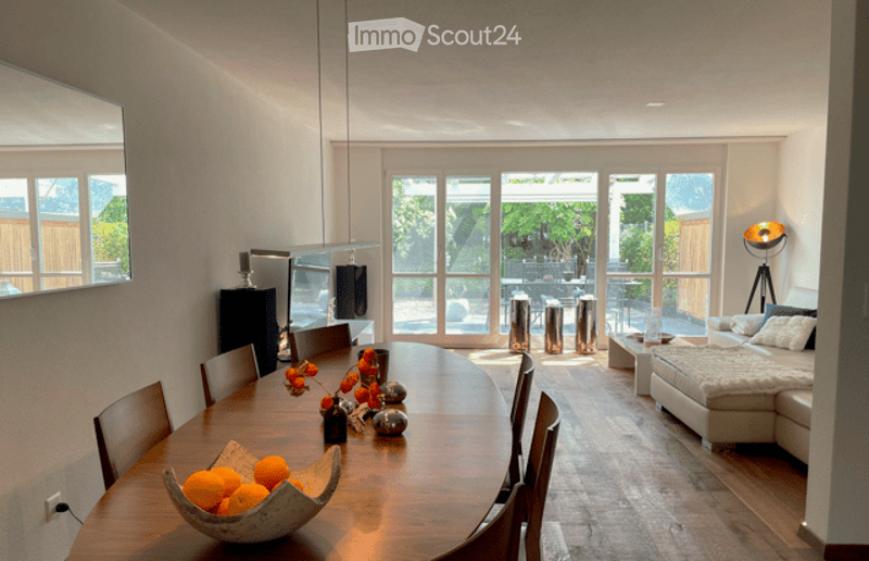 Open-plan living and dining area with modern furniture, large windows, and a view of the outdoor space.