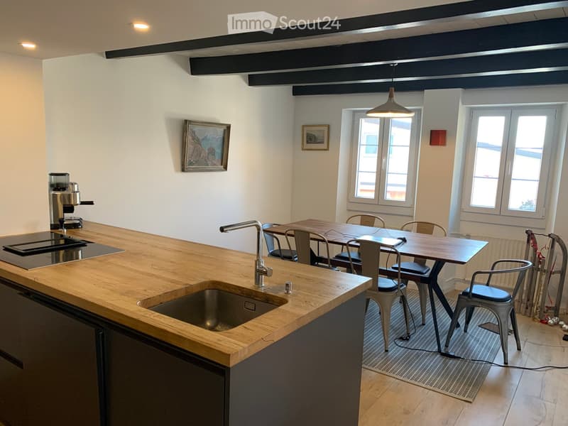 Modern kitchen with wooden countertops, stainless steel sink, coffee machine, and a dining area with a table and chairs.