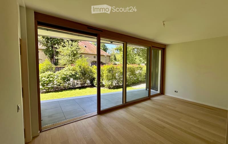 Empty room with wooden flooring, large sliding glass doors leading to a tiled patio and garden area.