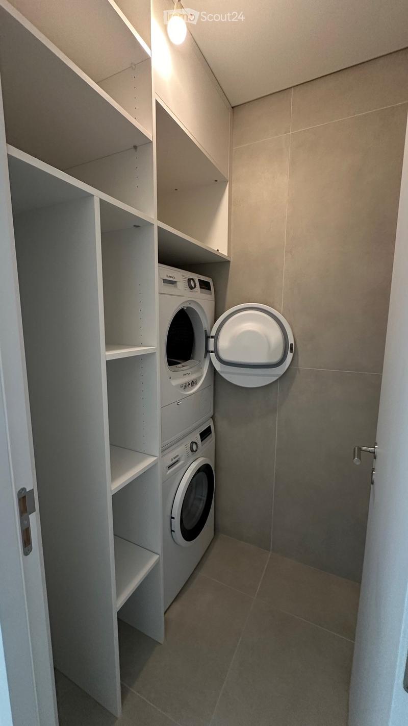 Modern bathroom with built-in white shelving, a stacked washing machine and dryer, and a toilet with an open lid.