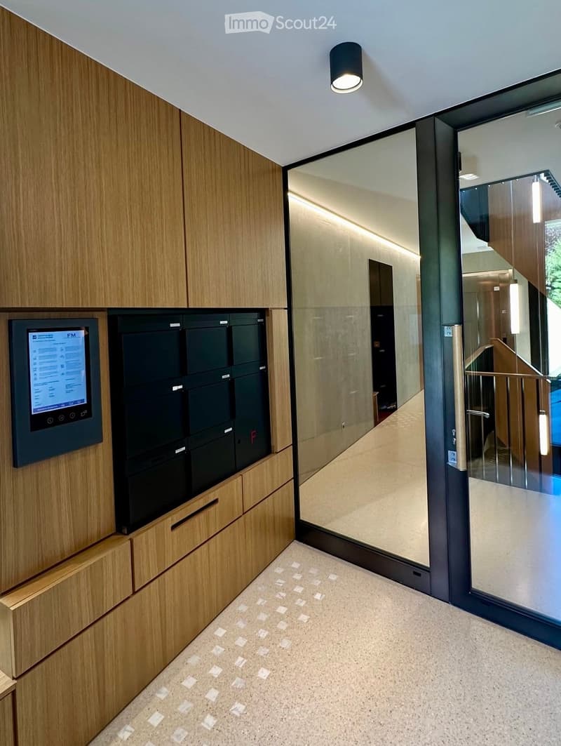 Modern hallway with wooden paneling, glass door, and digital display panel on the wall.