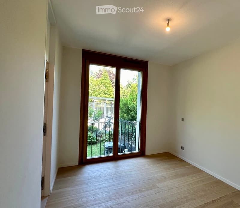 Empty room with wooden flooring, white walls, and a large sliding glass door leading to a balcony or outdoor area.