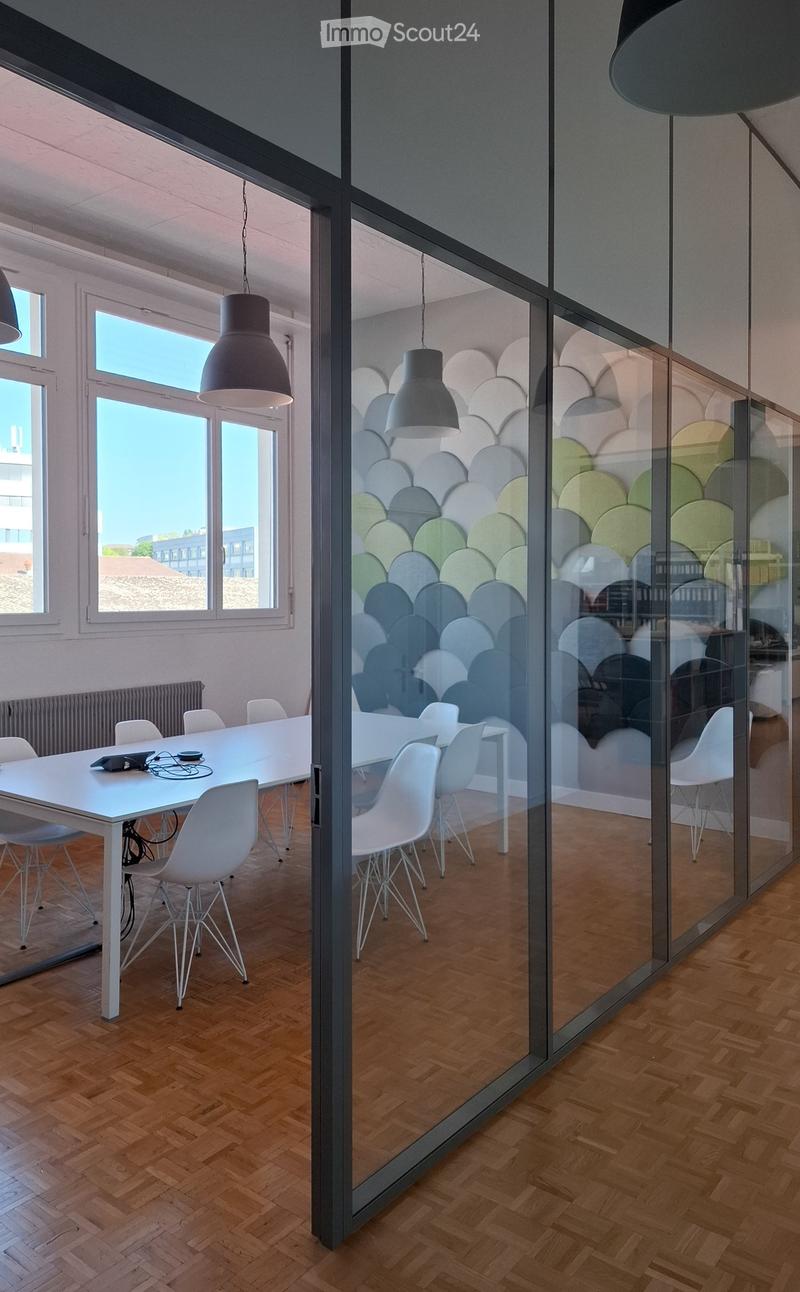 Modern office space with a long white table surrounded by white chairs, large windows, and glass partitions with decorative wall art.