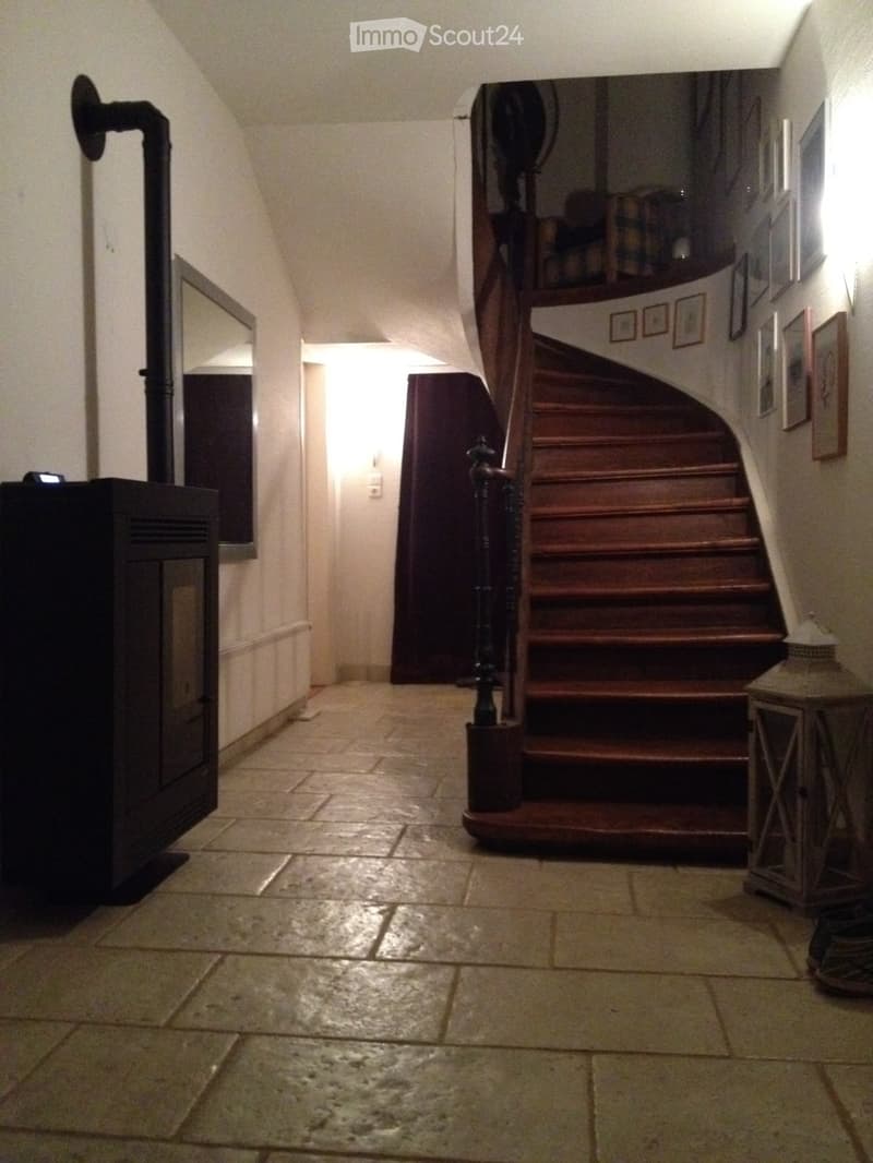 Hallway with a wooden staircase, tiled floor, and a black stove on the left side.